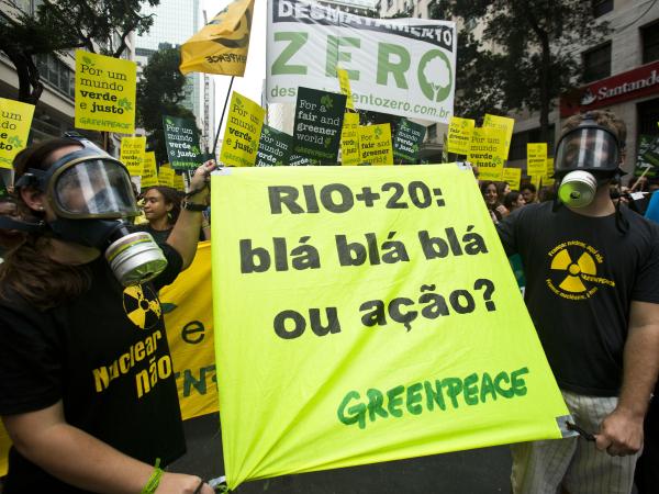 Greenpeace-Aktivisten auf der Demonstration in Rio anlässlich der Rio+20-Konferenz. Zwei Aktivisten mit Atemschutzmasken halten ein Banner mit der Aufschrift "Rio+20: blá, blá, blá ou ação? (Rio +20: bla, bla, bla oder Aktion?)